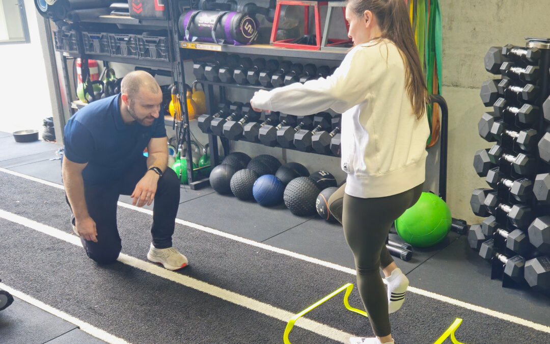A physiotherapist guiding a client through an agility drill over hurdles in the rehabilitation gym.