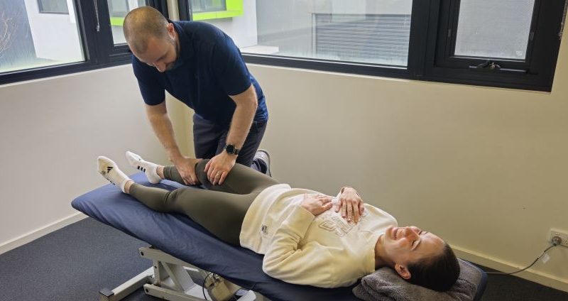 Physiotherapist performing a Lachman's test on a patient's knee to assess an ACL injury